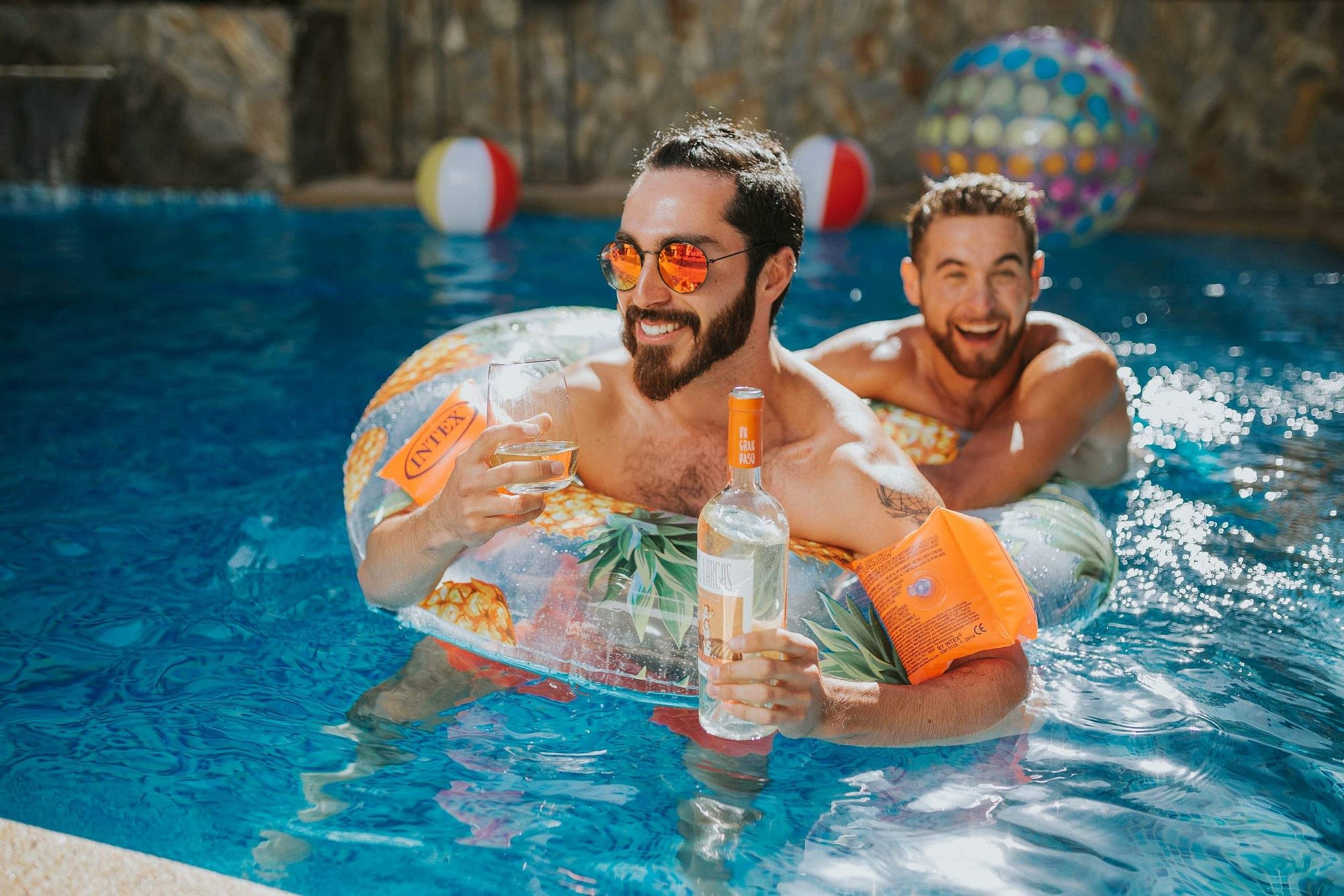 hombres jugando en la piscina con una botella de sauvignon blanc Piernas Largas en un día de verano